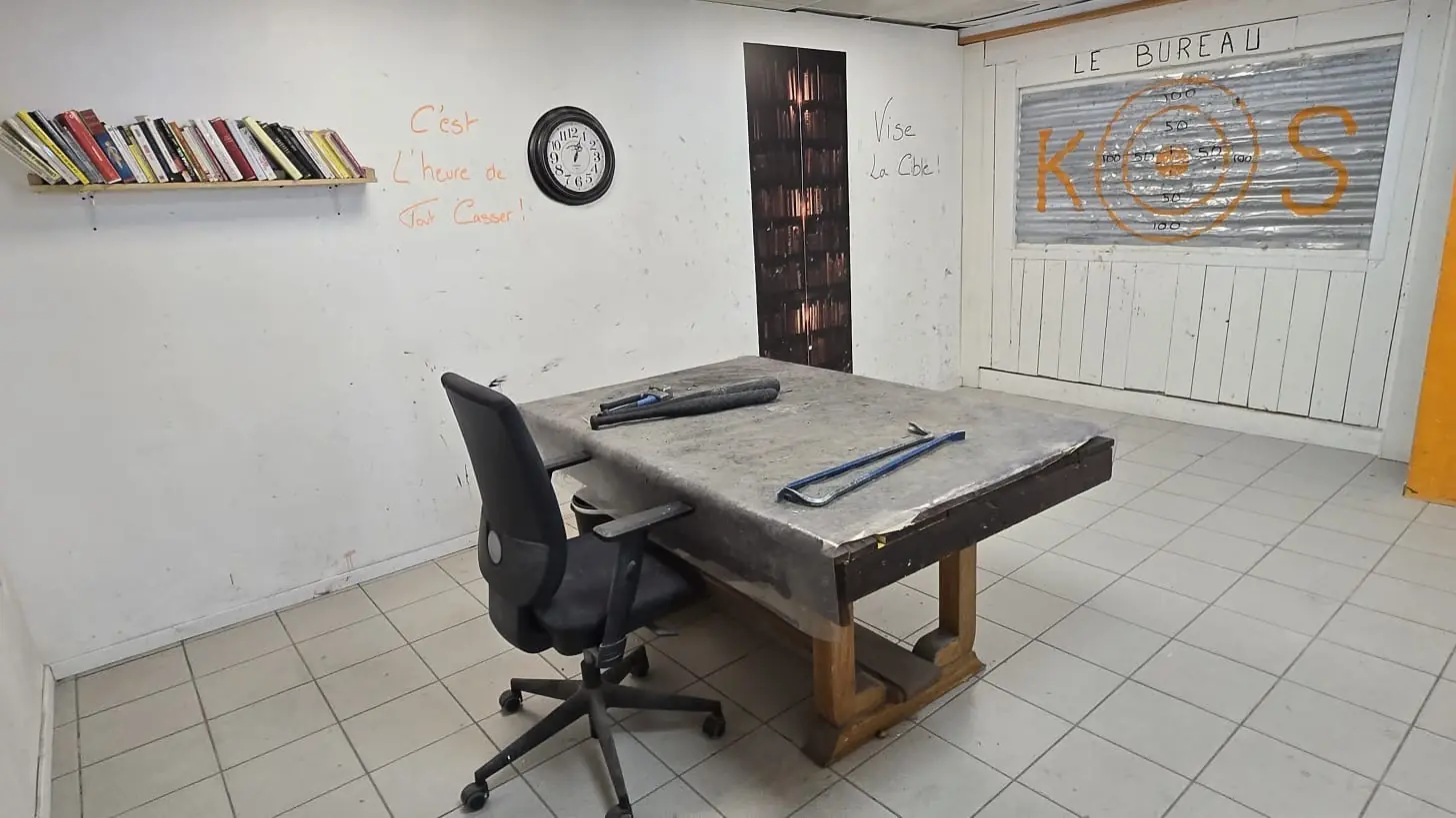 La salle bureau prête avant une session : table, chaise, étagère de livres, pied de biche et batte posés, cible peinte sur le rideau