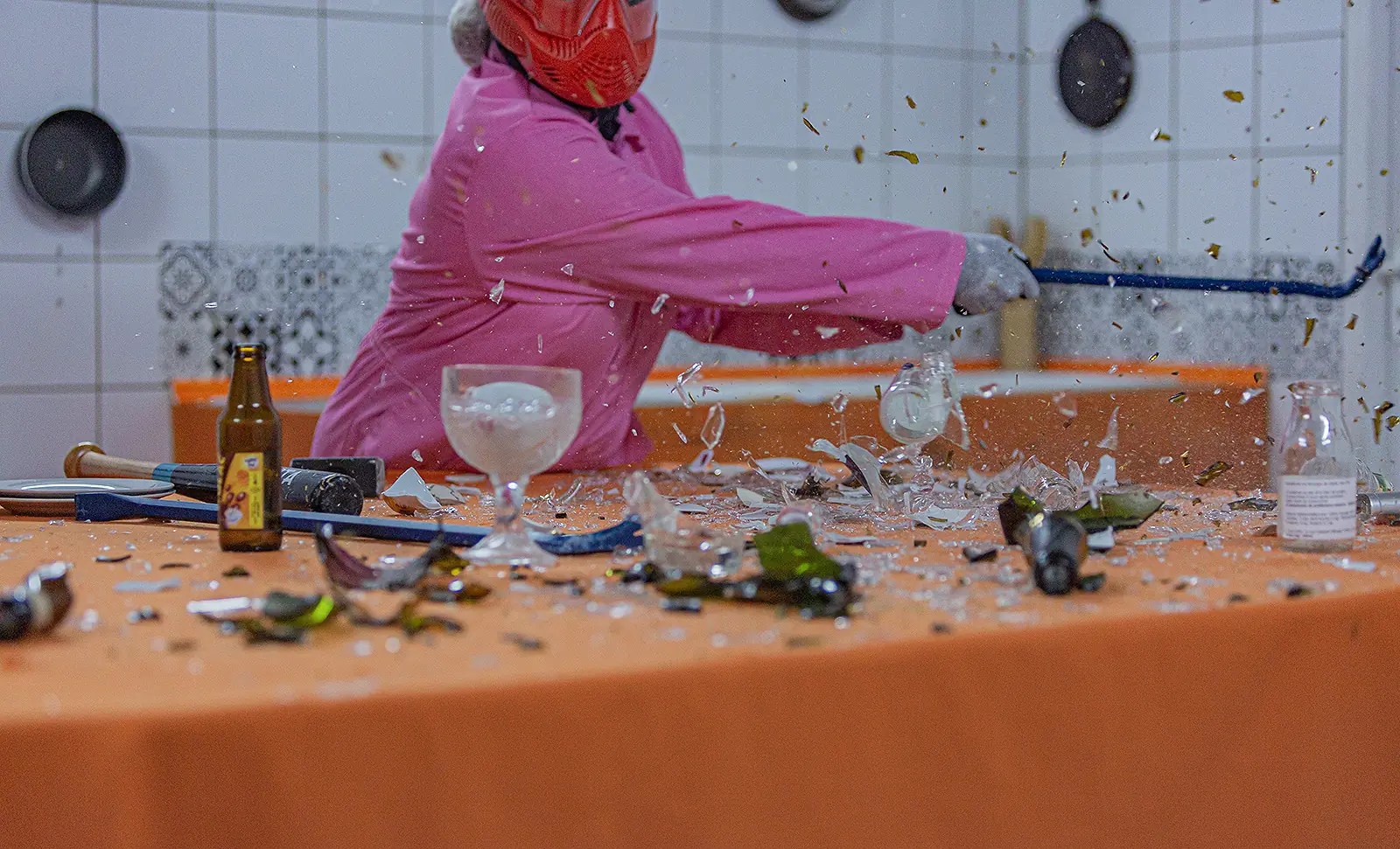 Une personne en combinaison rose fait voler les verres
d'un revers de batte sur la table de la cuisine