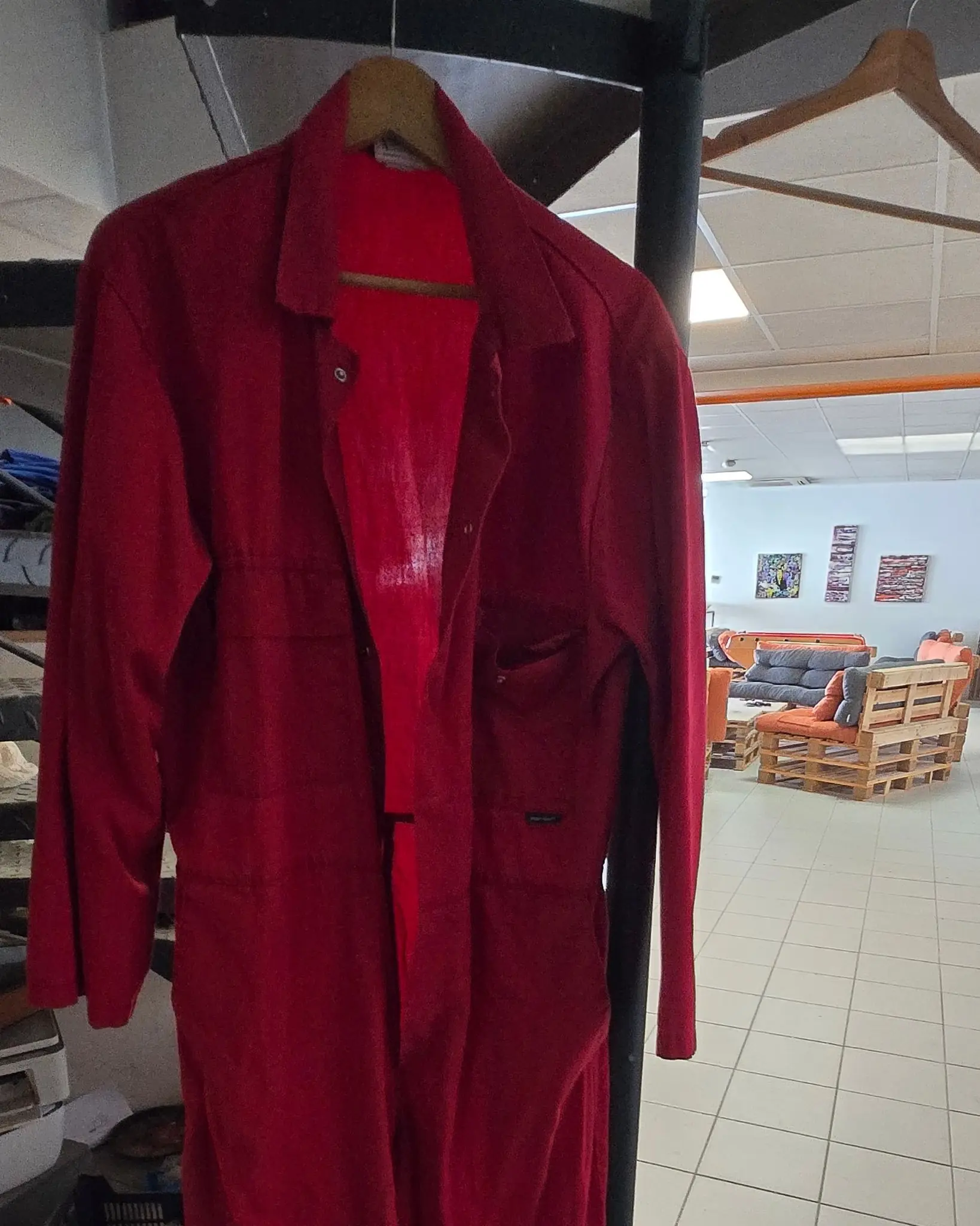 Combinaison intégrale rouge suspendue à un
cintre en bois, devant l'espace de décompression et
ses canapés en palettes