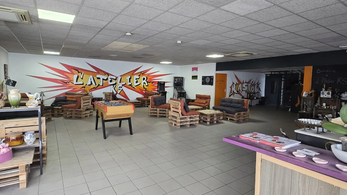 La salle principale de l'AtelierKS à La Rochelle :
canapés en palettes, baby-foot, flipper et jeu de
fléchettes devant le graff L'ATELIER KS