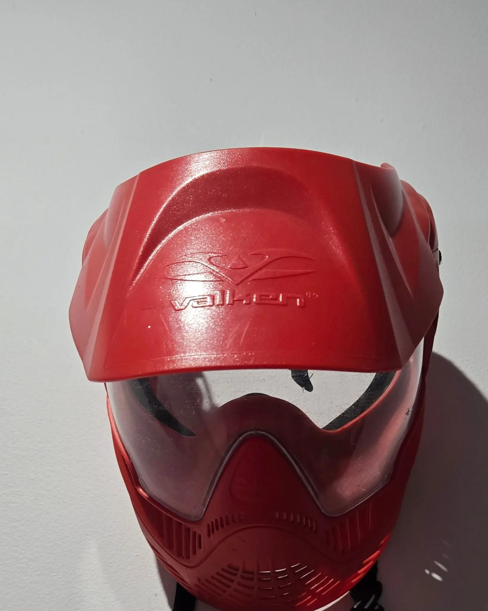 Casque à visière transparente rouge posé contre
un mur blanc, la protection du visage fournie avant
chaque séance