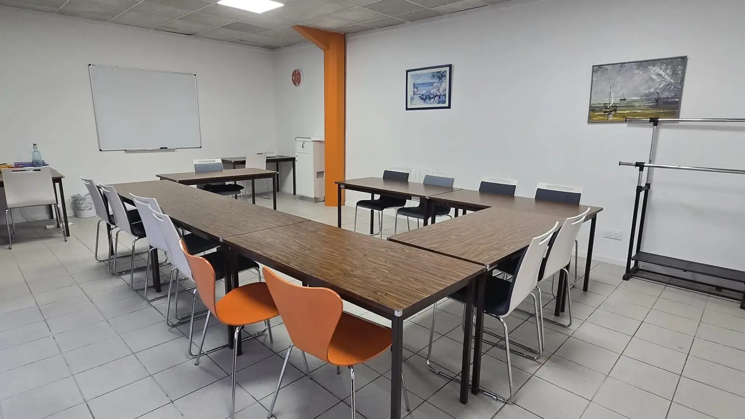 La salle de réunion où démarre l'escape game à
La Rochelle : tables en U, douze chaises blanches et
orange, tableau blanc et pilier orange